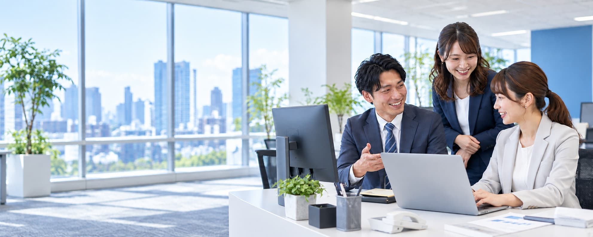 明るい会社のオフィスで、20代中盤から後半の男性1人と女性2人がPCを使い楽しそうに仕事をするイメージ